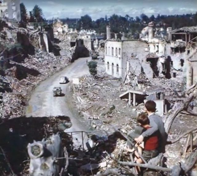 Doi baieti privind dintr-un copac cum soldatii americani merg prin Saint-Lo, Franta