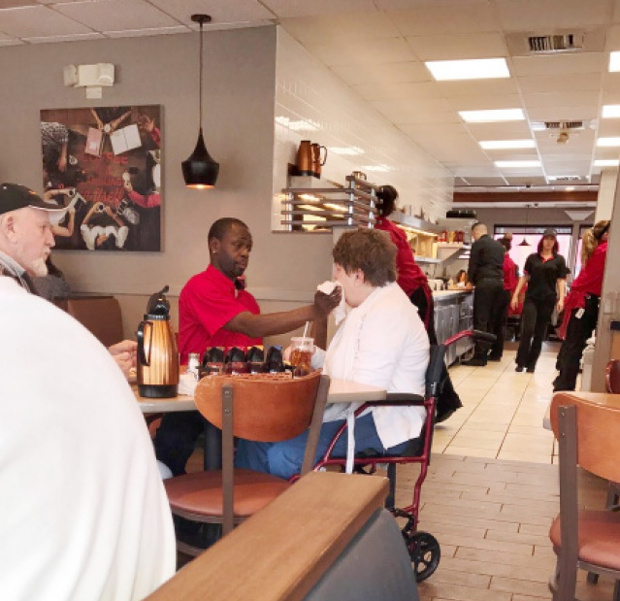 Un ospatar ajuta o femeie cu dizabilitati sa manance, pentru a-i permite si sotului ei sa ia masa