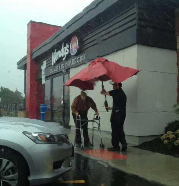 Angajatul unui restaurant insoteste un batran la masina si il protezeaja de ploaie cu o umbrela luata de la terasa localului