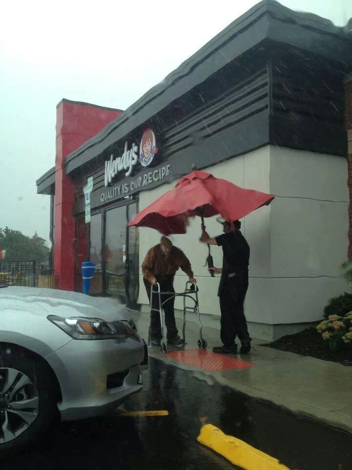 Un angajat de la un fast-food ia o umbrela de la o masa, pentru a conduce un batran la masina sa, in timp ce ploua