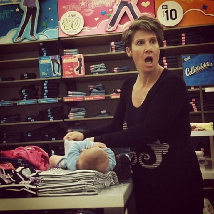 O mama isi schimba copilul pe hainele de pe raftul unui magazin